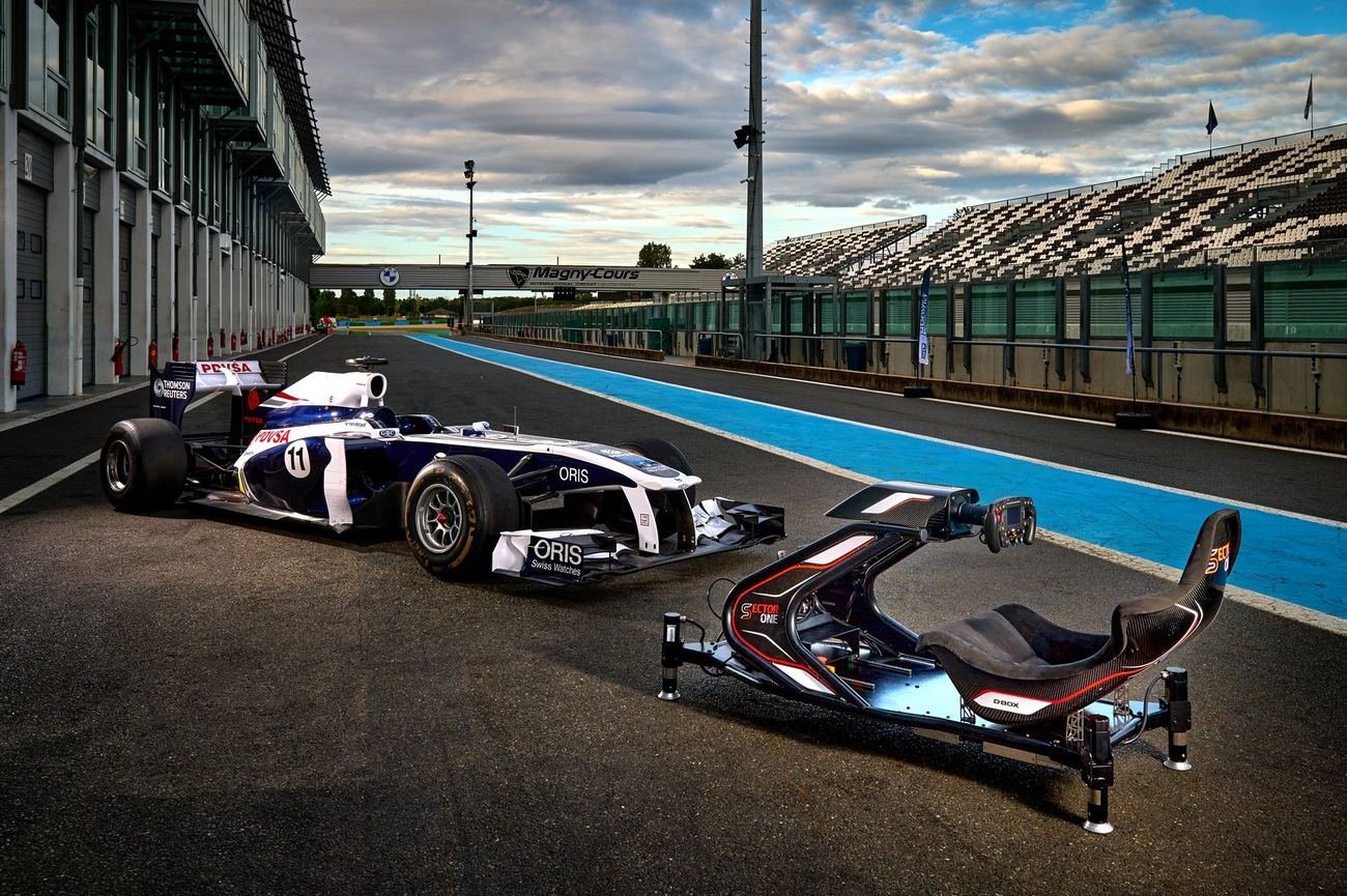 A Sector One simulator chassis beside a Formula 1 car in the pit lane